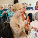 A woman holds a microphone while seated next to other women at a table